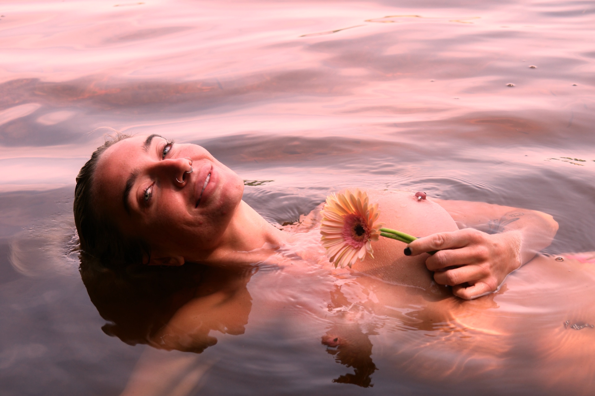 A woman floating in rosy water holding a pink gerbera