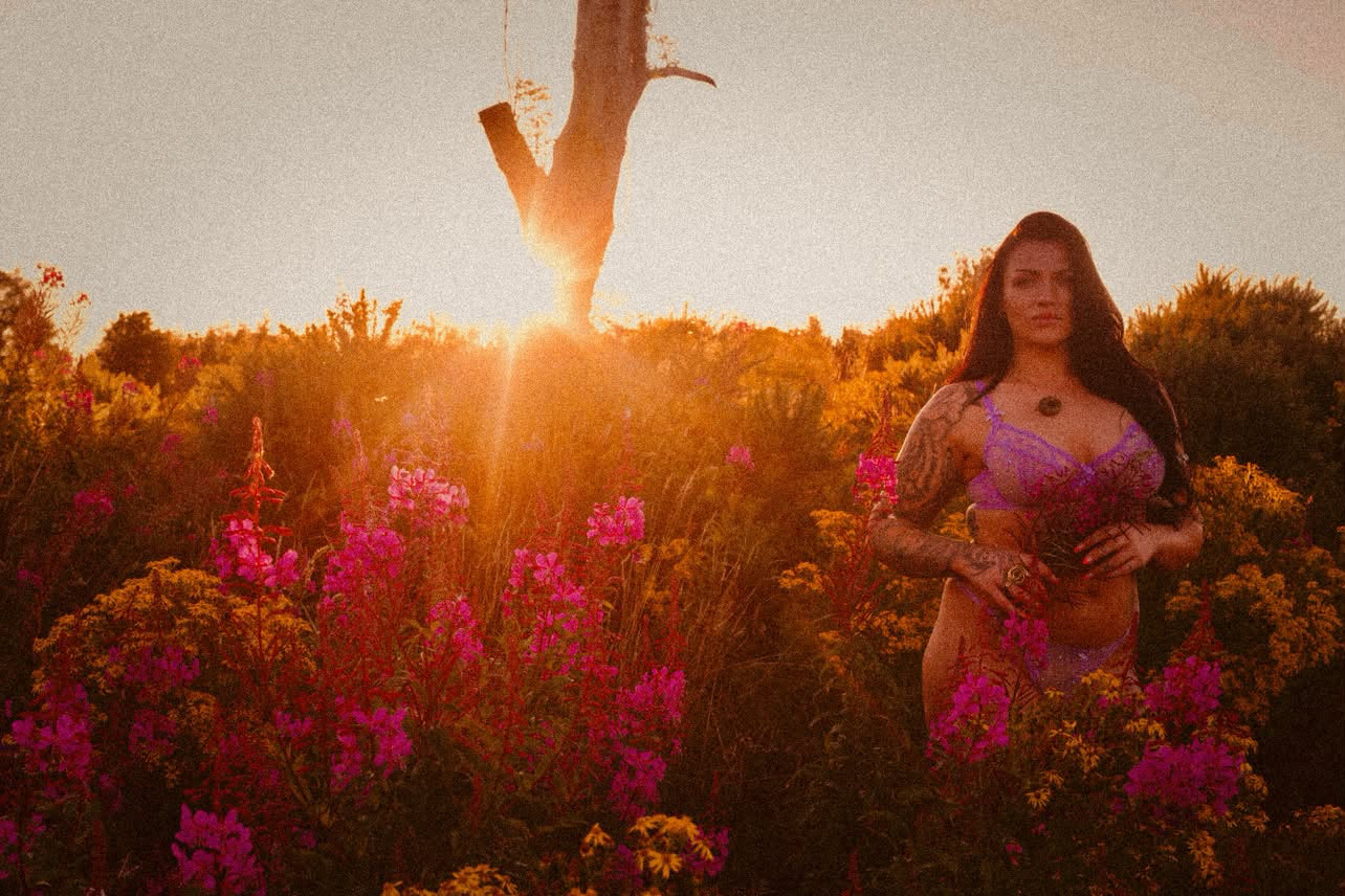 Woman in lilac lace standing among fireweed at golden sunset
