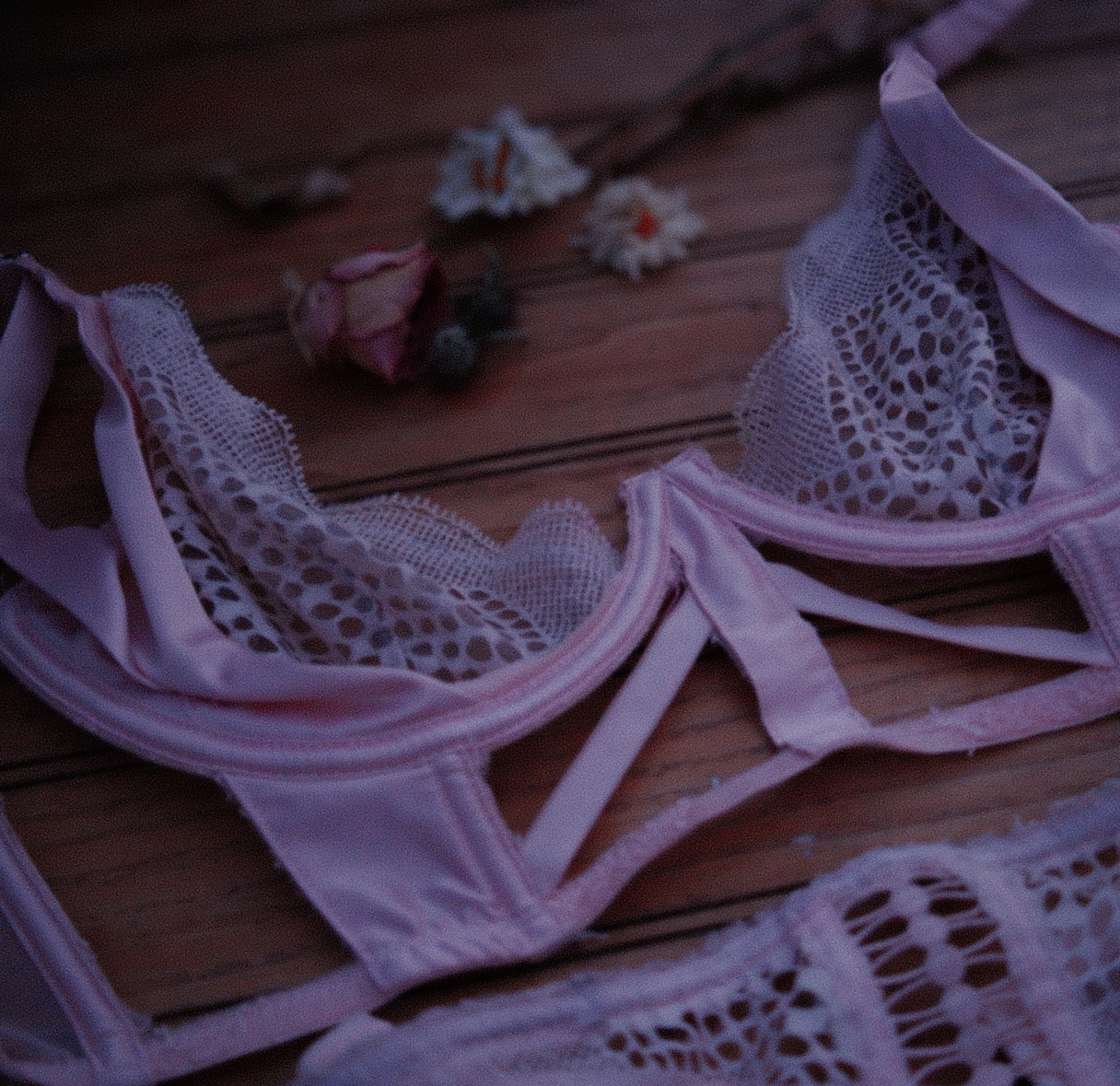Pink lace lingerie set laid on a wooden floor with a rosebud